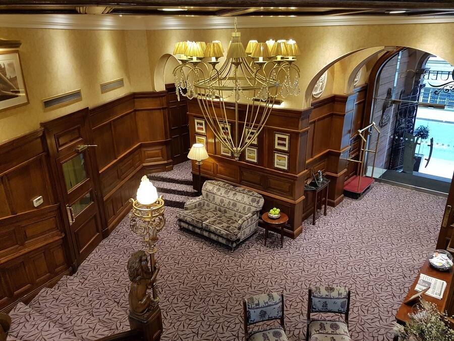 A lobby with a patterned carpet, a sofa, a chandelier, and a statue.