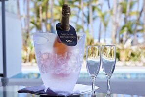 A welcome sign on an ice bucket with two glasses beside it, set against a poolside view.