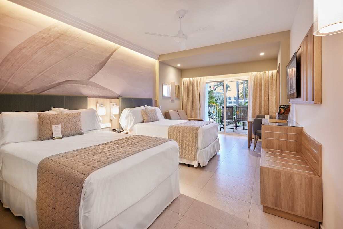 A hotel room with two beds, a desk, and a balcony with a view.