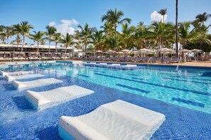 A swimming pool with lounge chairs and umbrellas, surrounded by palm trees.
