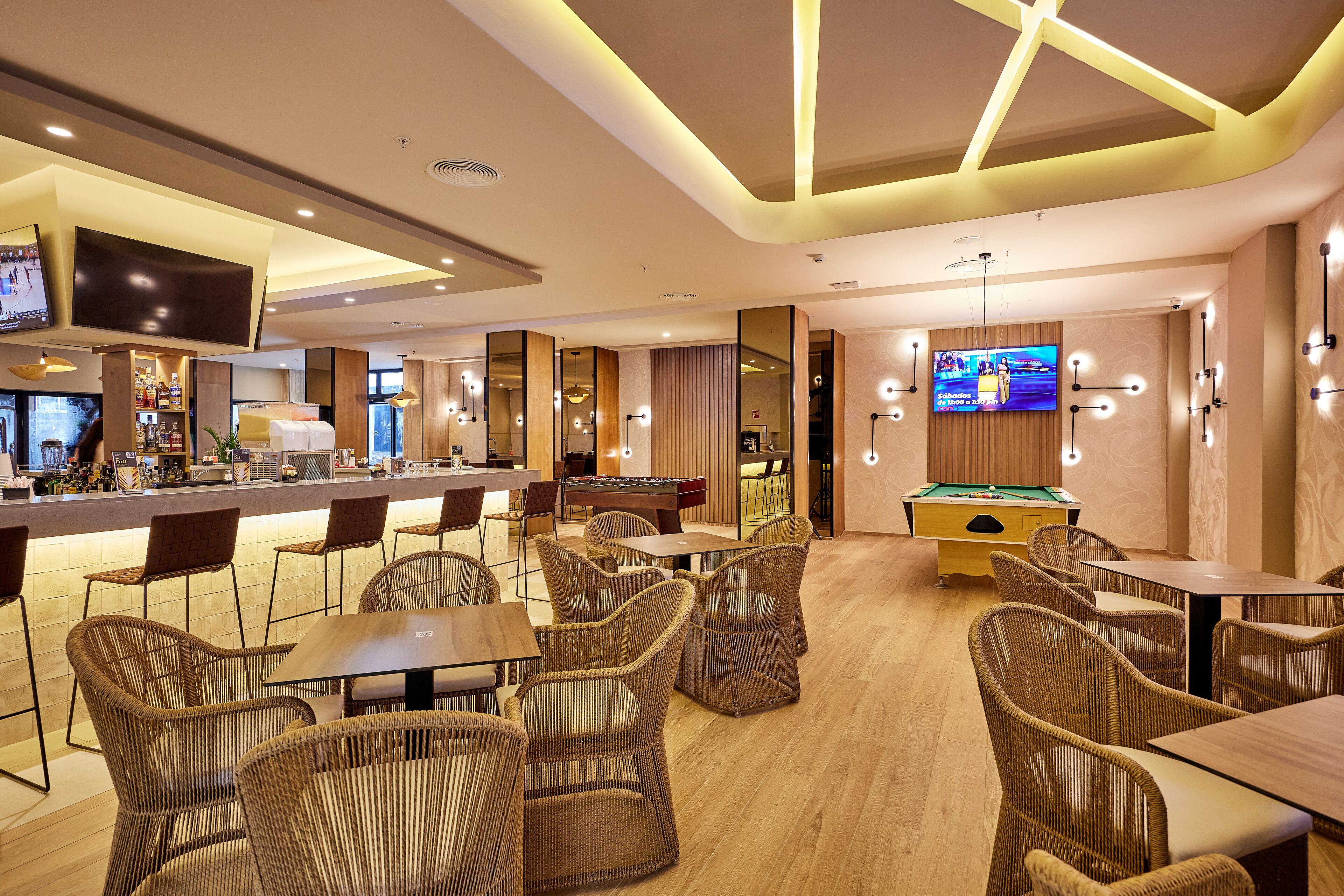 A modern bar area with a pool table, comfortable wicker chairs, and a television screen.