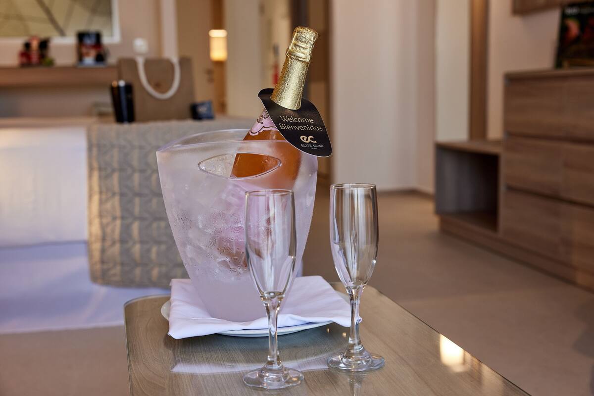 A bottle of champagne with a label, two glasses, and a large ice bucket on a wooden table.