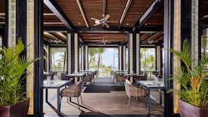 An outdoor dining area with wooden flooring, tables, chairs, and ceiling fans. - Hotel Riu Palace Macao - Adults Only - All Inclusive (Punta Cana)