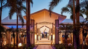 A modern building with a central entrance, surrounded by palm trees and a pathway leading to the entrance. - Hotel Riu Palace Macao - Adults Only - All Inclusive (Punta Cana)