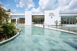 A modern spa building with a clear pool area, palm trees, and a clear sky. - Hotel Riu Palace Macao - Adults Only - All Inclusive (Punta Cana)