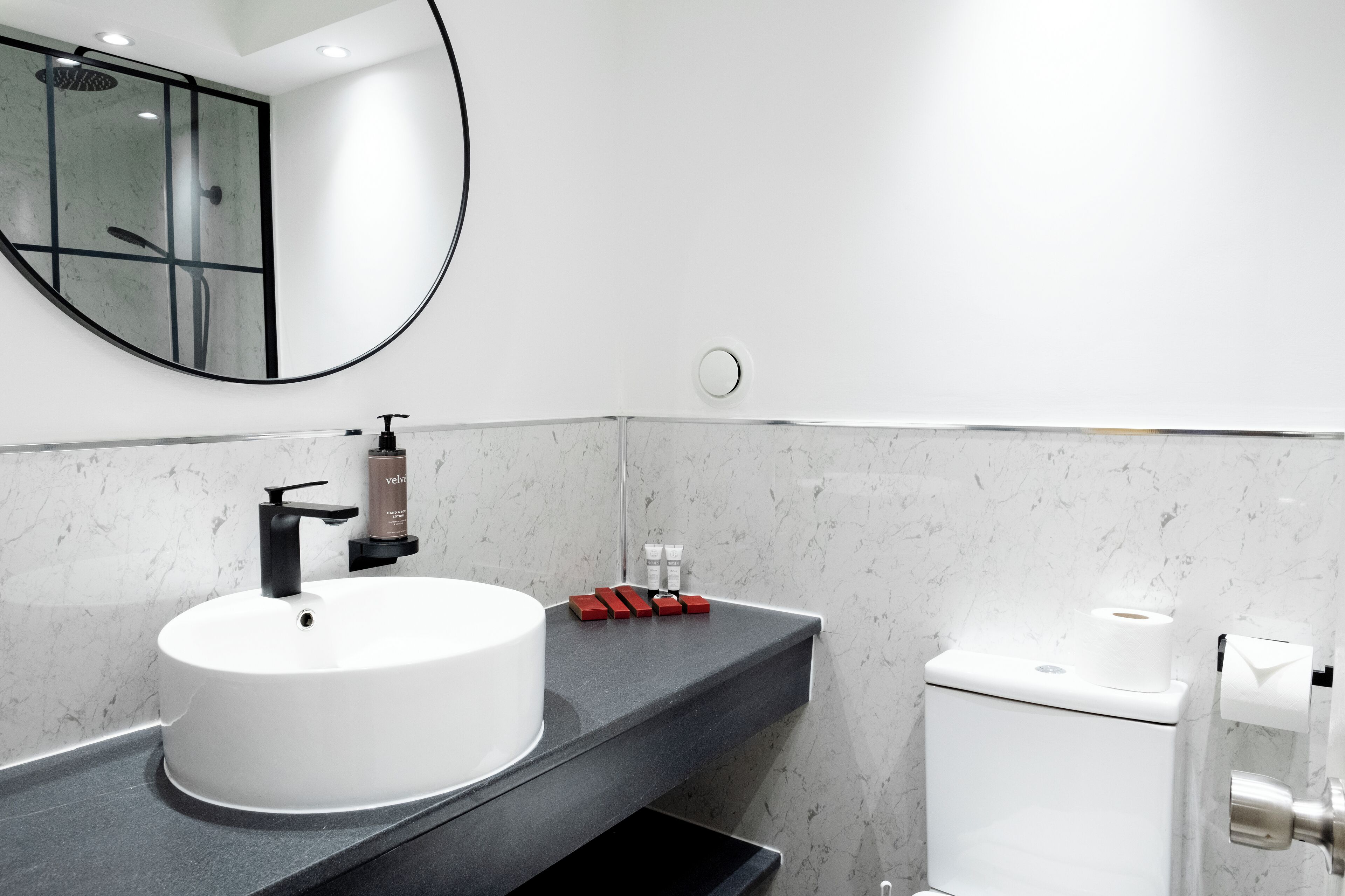 Une salle de bain moderne avec un lavabo blanc, un robinet noir et un miroir rond.