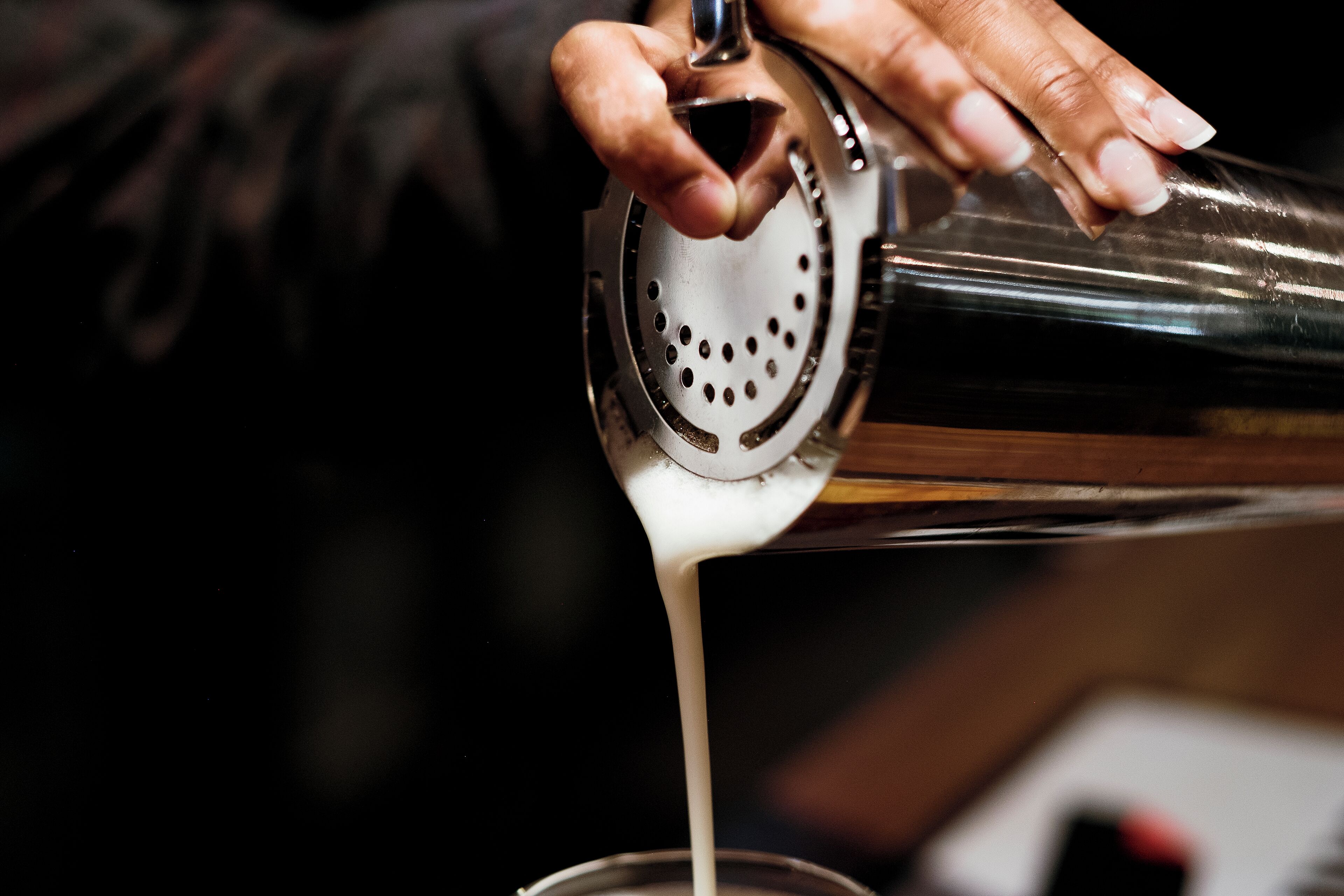 Een hand giet een vloeistof uit een cocktailshaker in een glas.