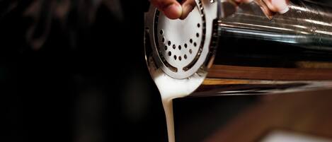 Een hand giet een vloeistof uit een cocktailshaker in een glas.
