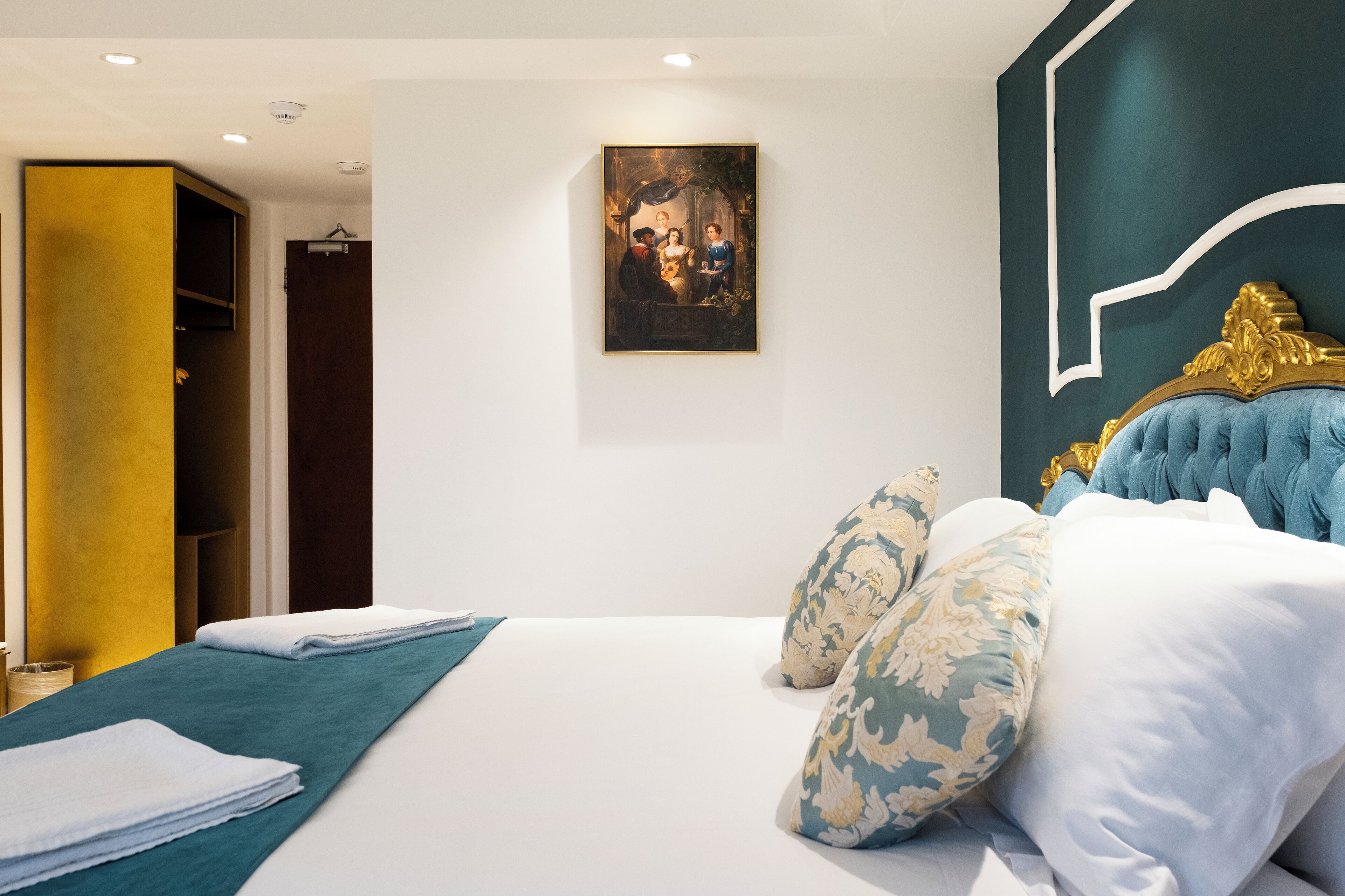 A modern hotel room with a large bed, a painting on the wall, and a view of the hallway.