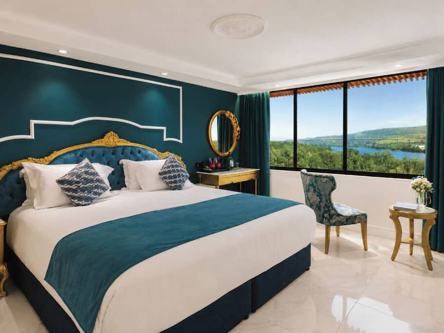 A hotel room with a large bed, a view of the outdoors, a desk, and a chair.