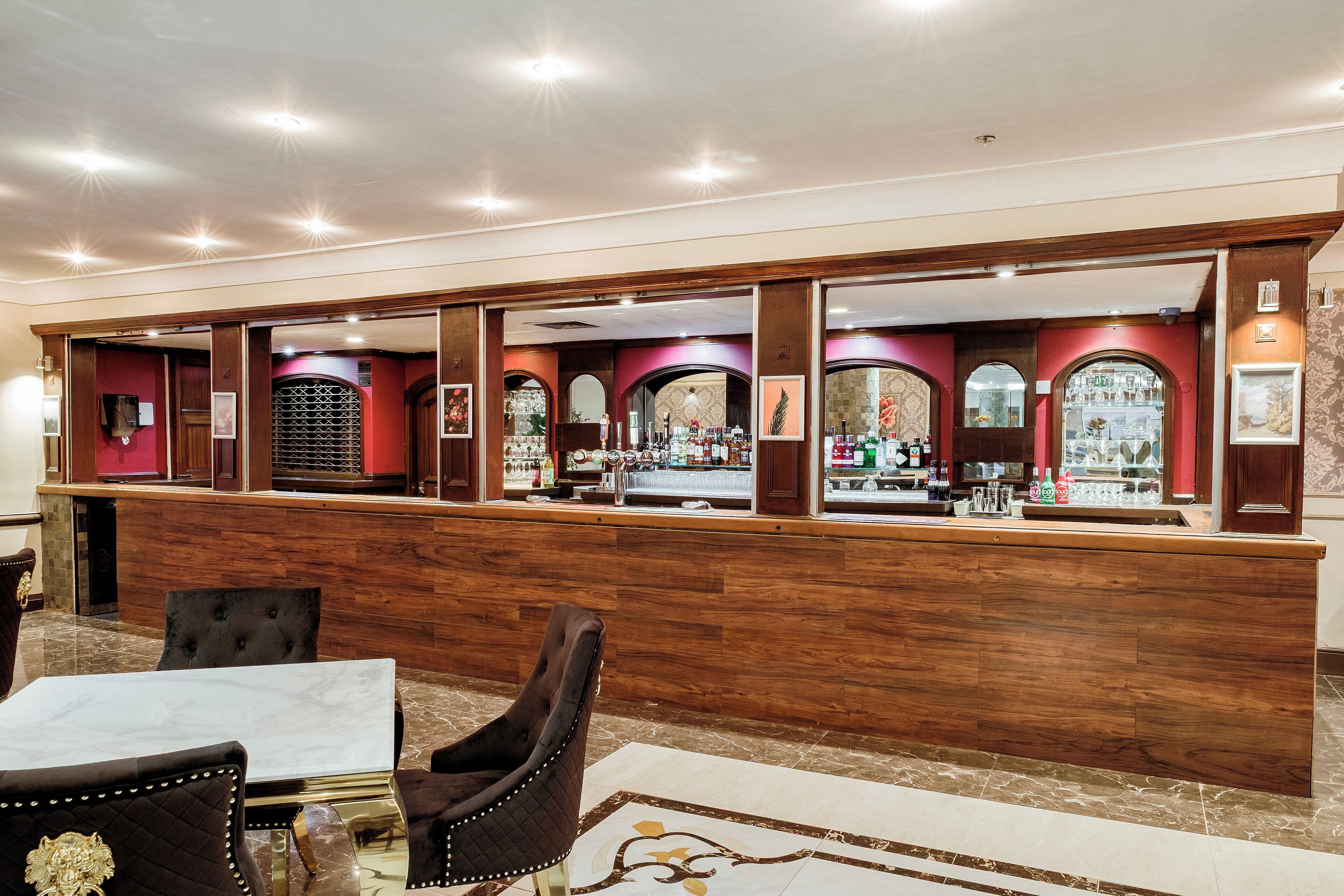 A bar area with a wooden counter, marble-topped tables, and cushioned chairs.