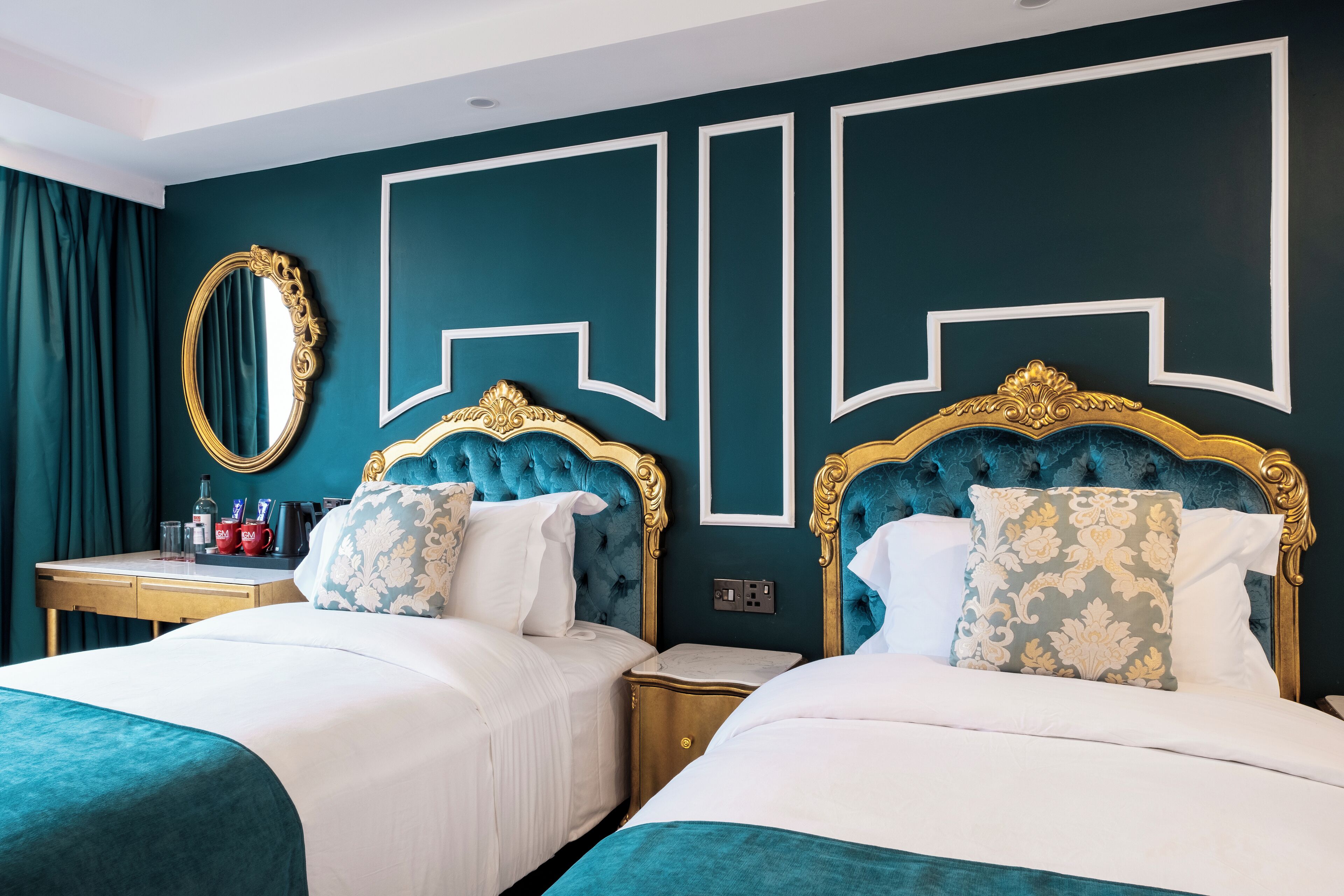 Une chambre d’hôtel avec deux lits, un grand miroir et un mur orné de motifs géométriques.