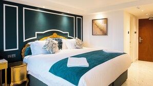 Een netjes opgemaakt bed met een blauwgroene deken, een gouden hoofdbord en kussens met bloemenprint.