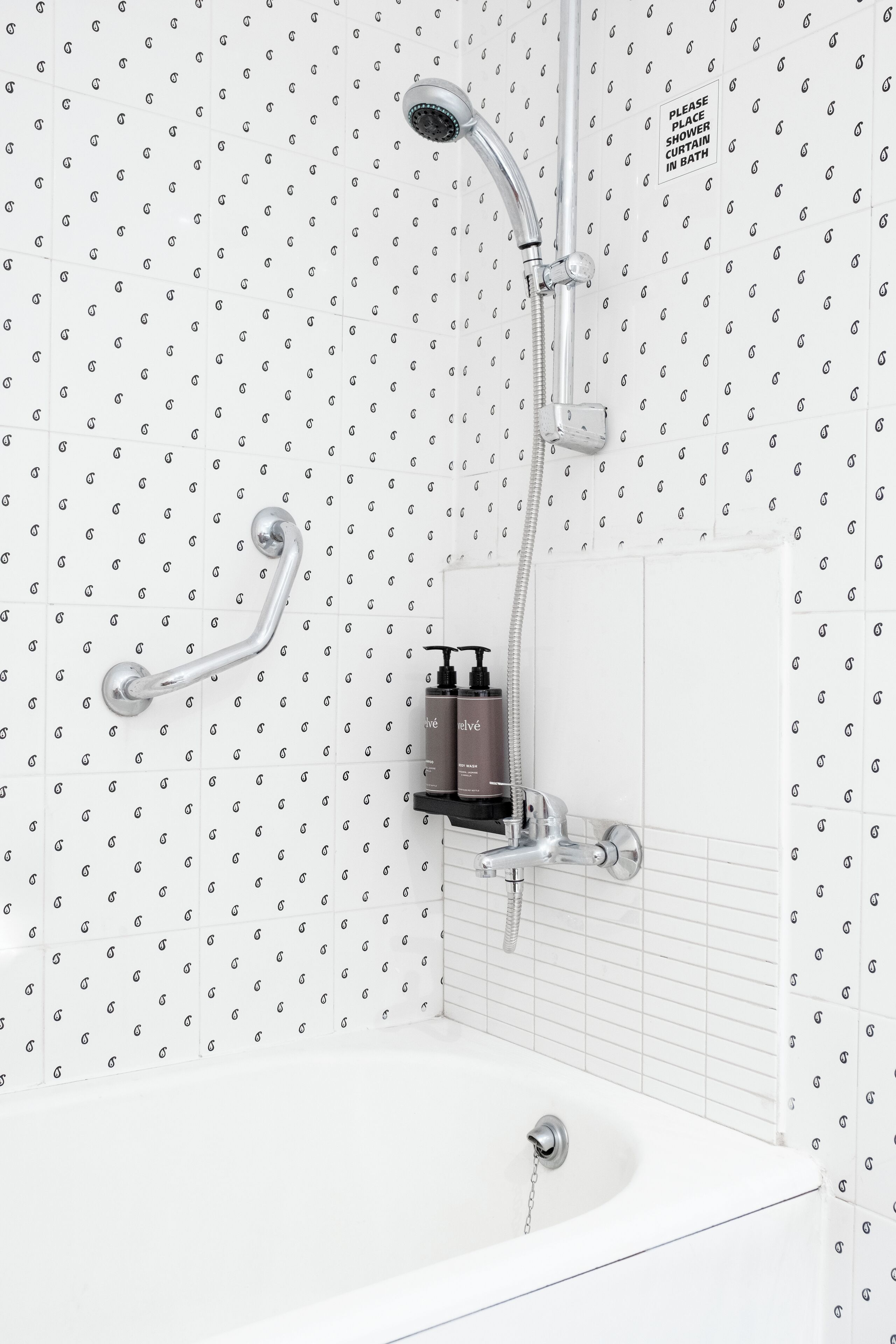A modern bathroom with a shower, grab bar, and a soap dispenser on the wall.
