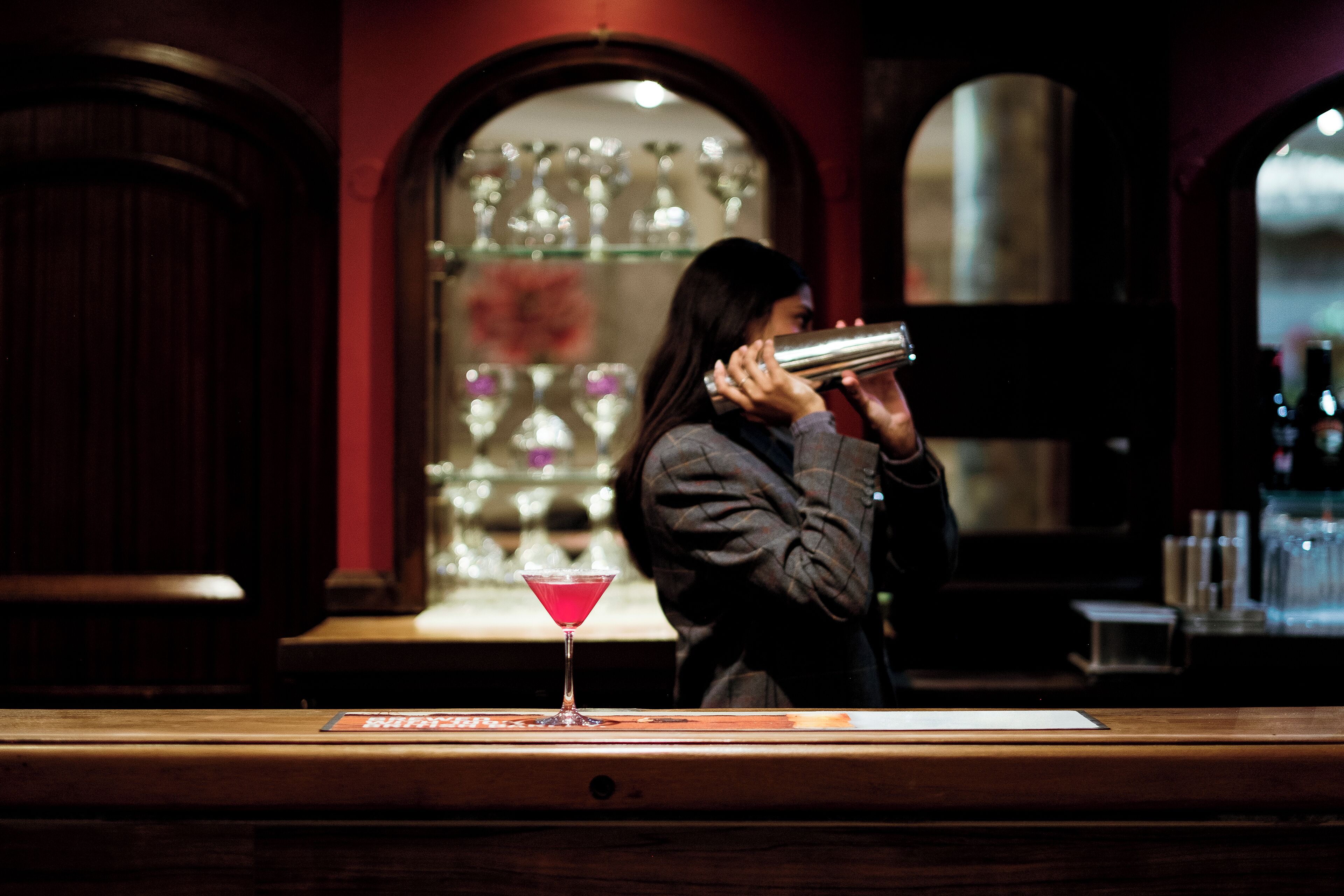Een bar met een martini glas op een onderzetter, een fles drank en een persoon die een fles vasthoudt.