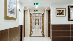Een hotelgang met een marmeren vloer, houten lambrisering en ingelijste kunstwerken.
