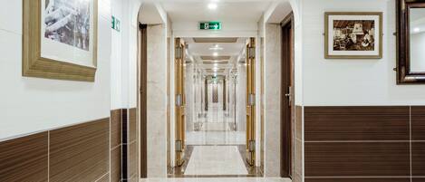 Een hotelgang met een marmeren vloer, houten lambrisering en ingelijste kunstwerken.