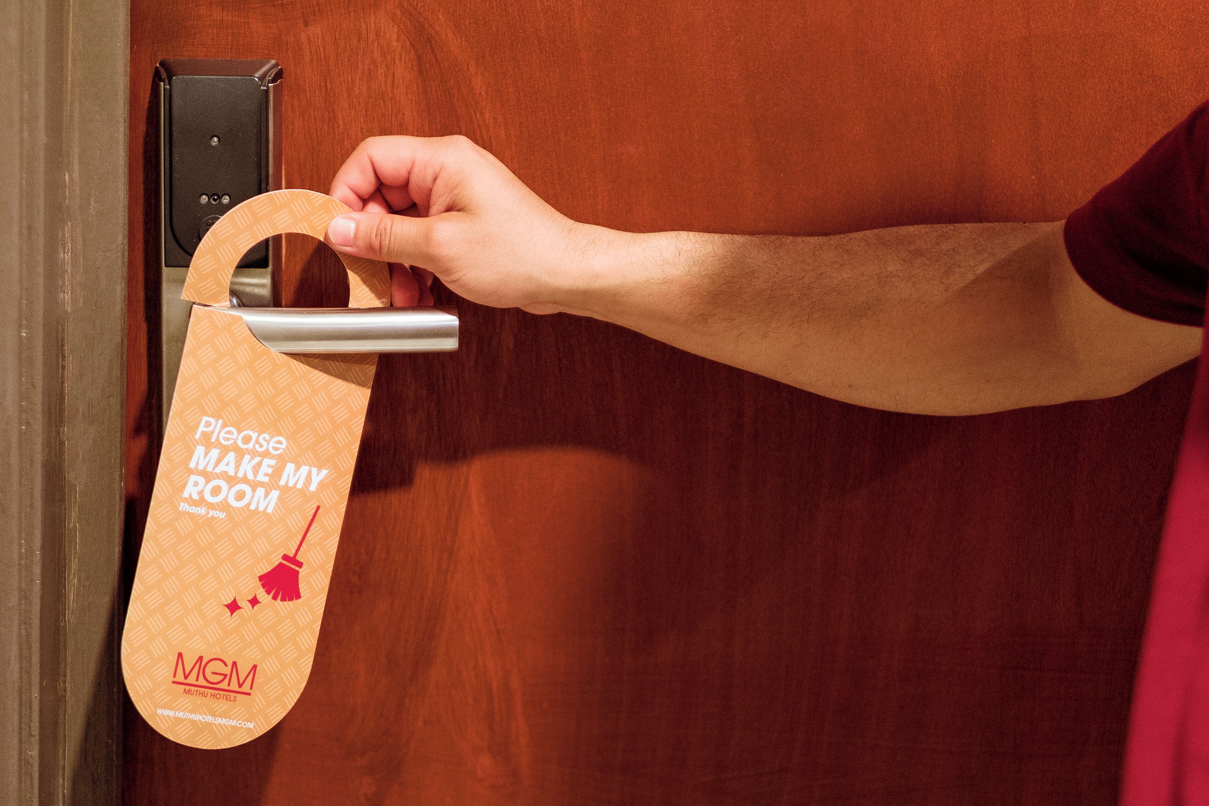 A hand holding a "Please Make My Room" sign at a hotel door.