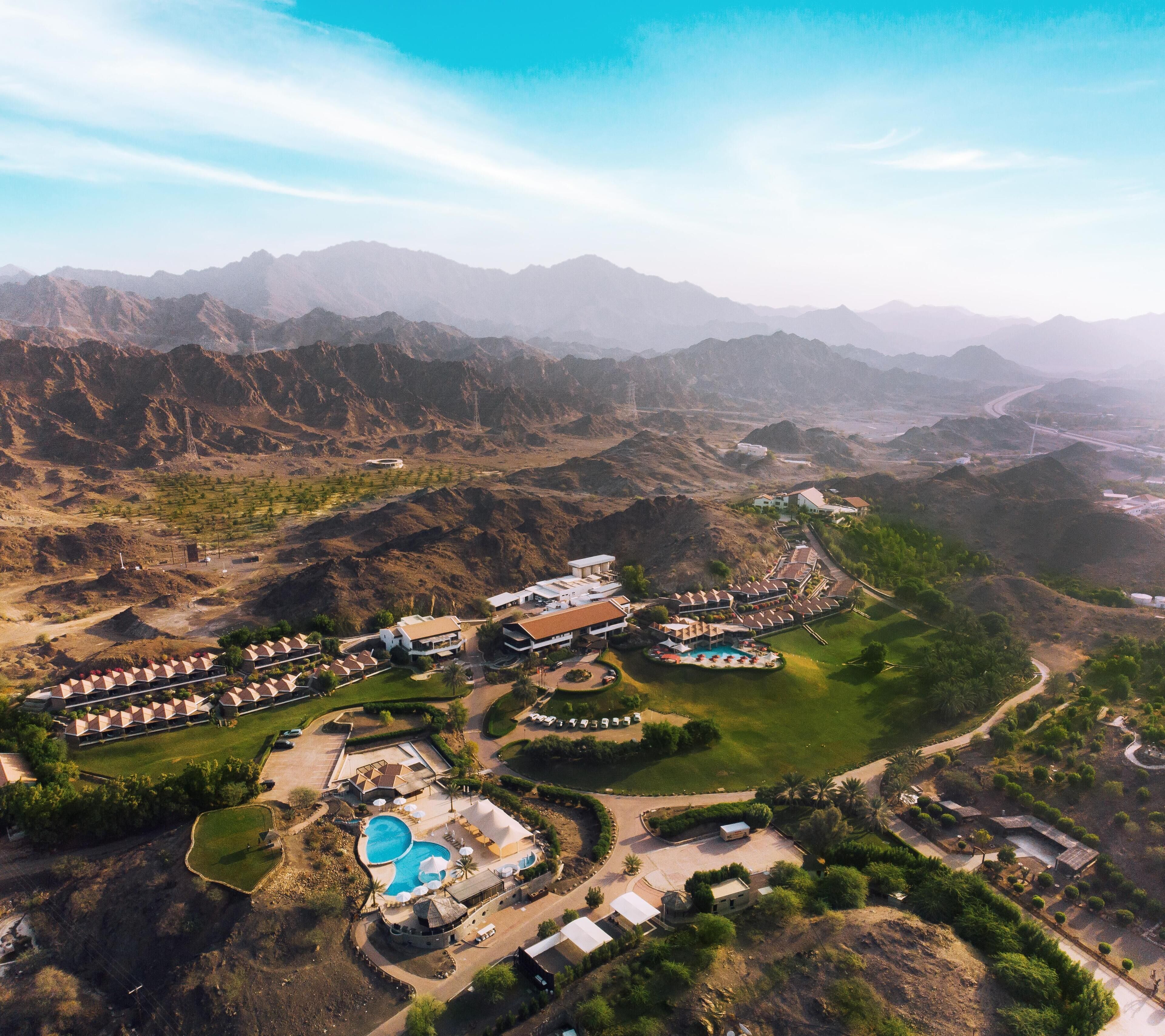 Vista aérea de un resort con varias edificaciones, una piscina y zonas ajardinadas.