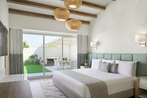 A modern hotel room with a large bed, a dining area with a table and chairs, and a view of a green lawn. - JA Hatta Fort Hotel (Hatta)