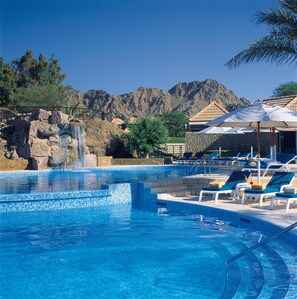 A swimming pool with a waterfall feature, lounge chairs, and a mountainous backdrop. - JA Hatta Fort Hotel (Hatta)