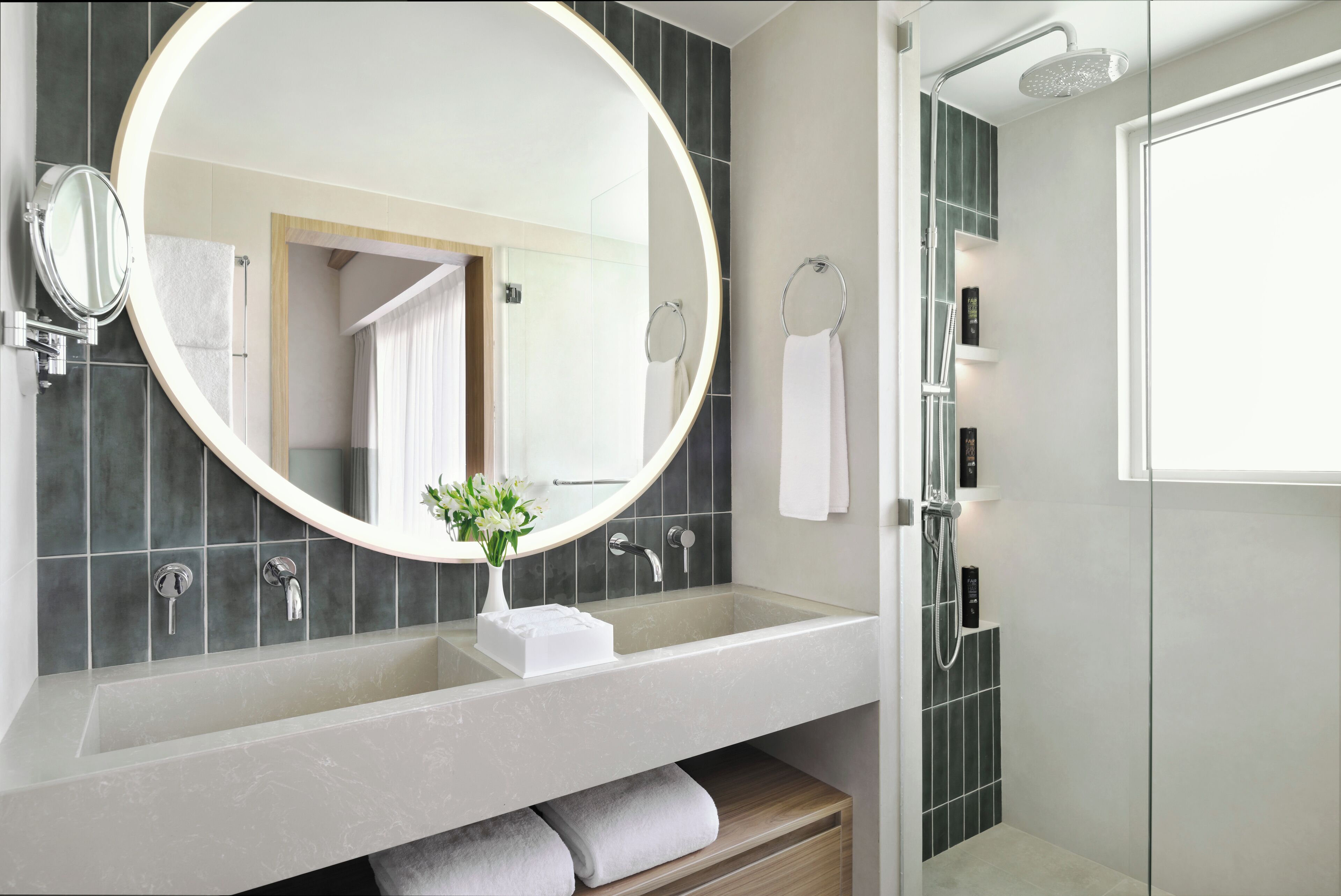 A modern bathroom with a large round mirror, a sink with a white towel, and a shower area.