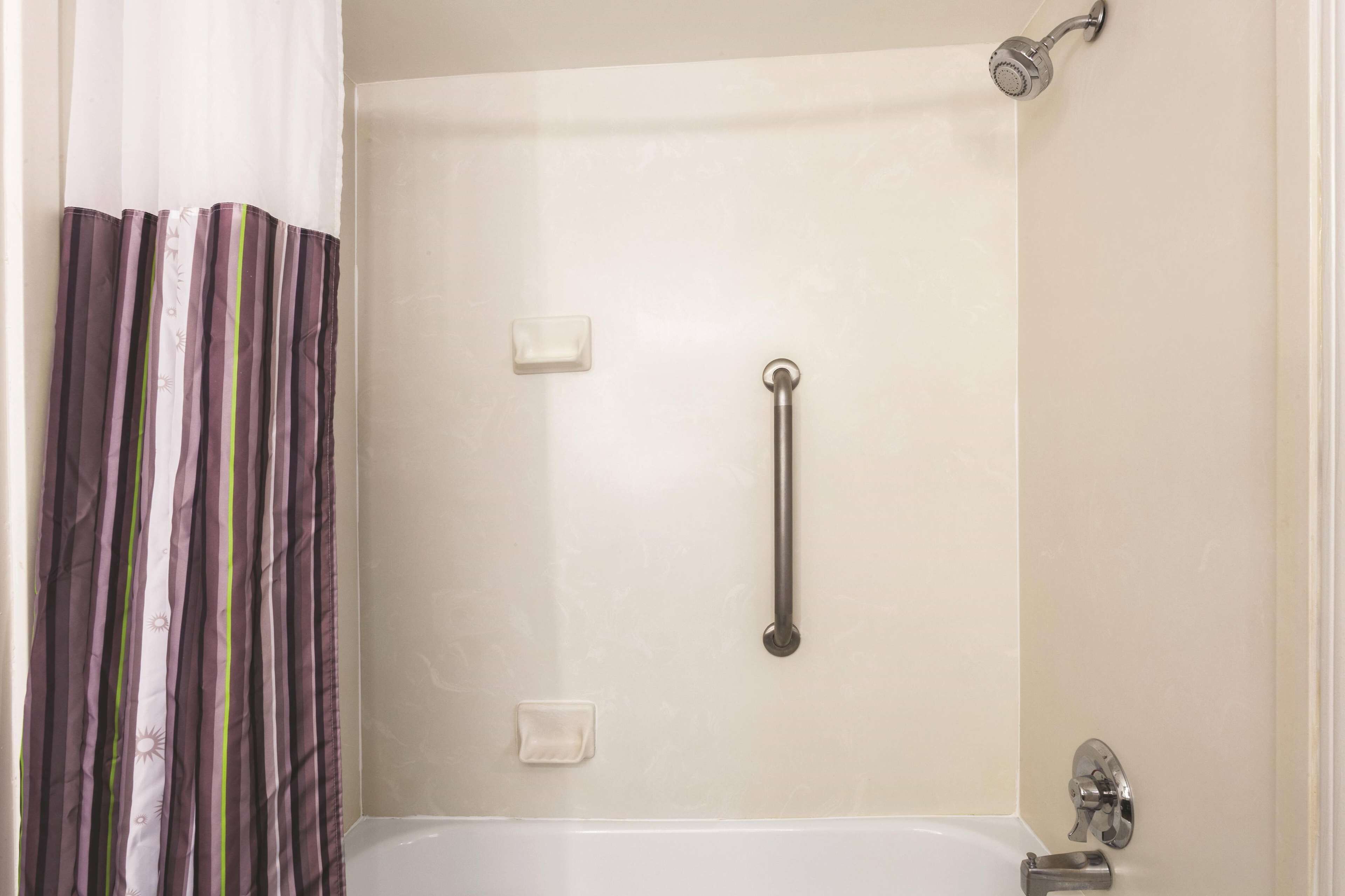 A bathroom with a bathtub, a shower, and a handrail.