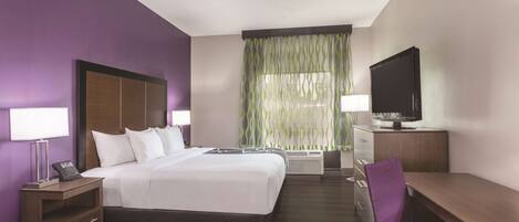A hotel room with a bed, a desk, a television, and a window with curtains.