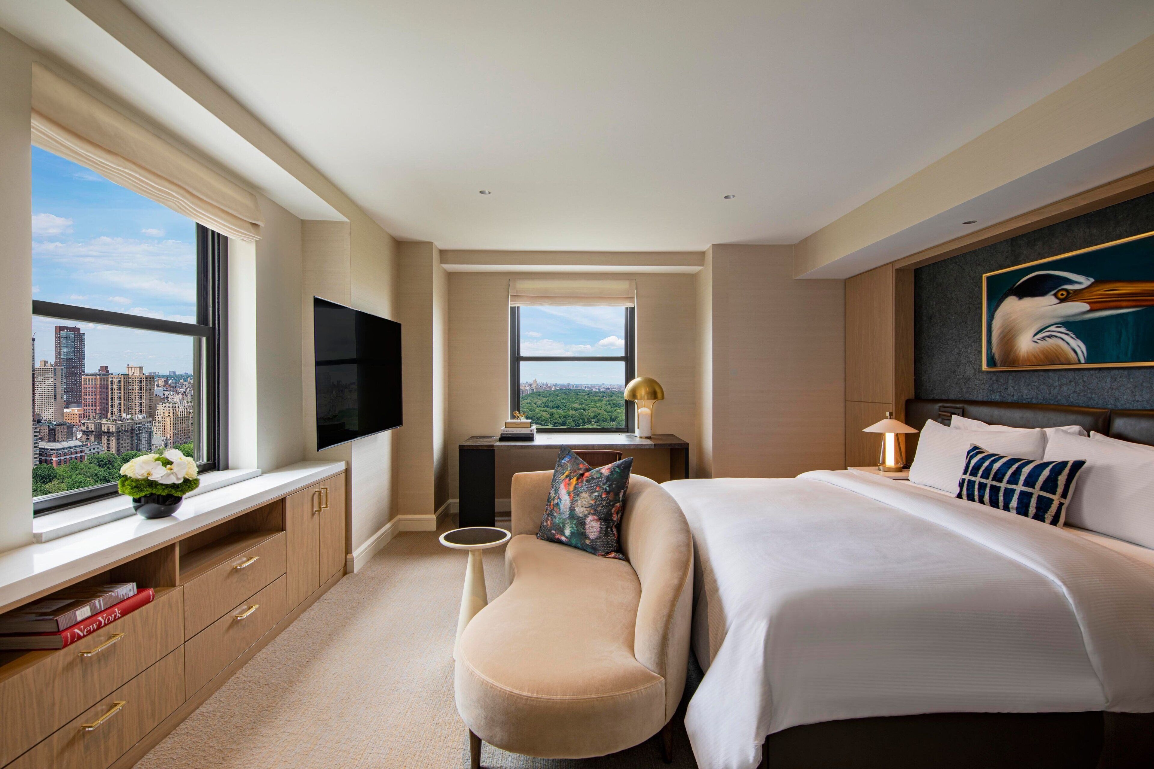 Une chambre d’hôtel moderne avec un grand lit, un bureau avec une télévision, une vue sur la ville et un tableau au mur.