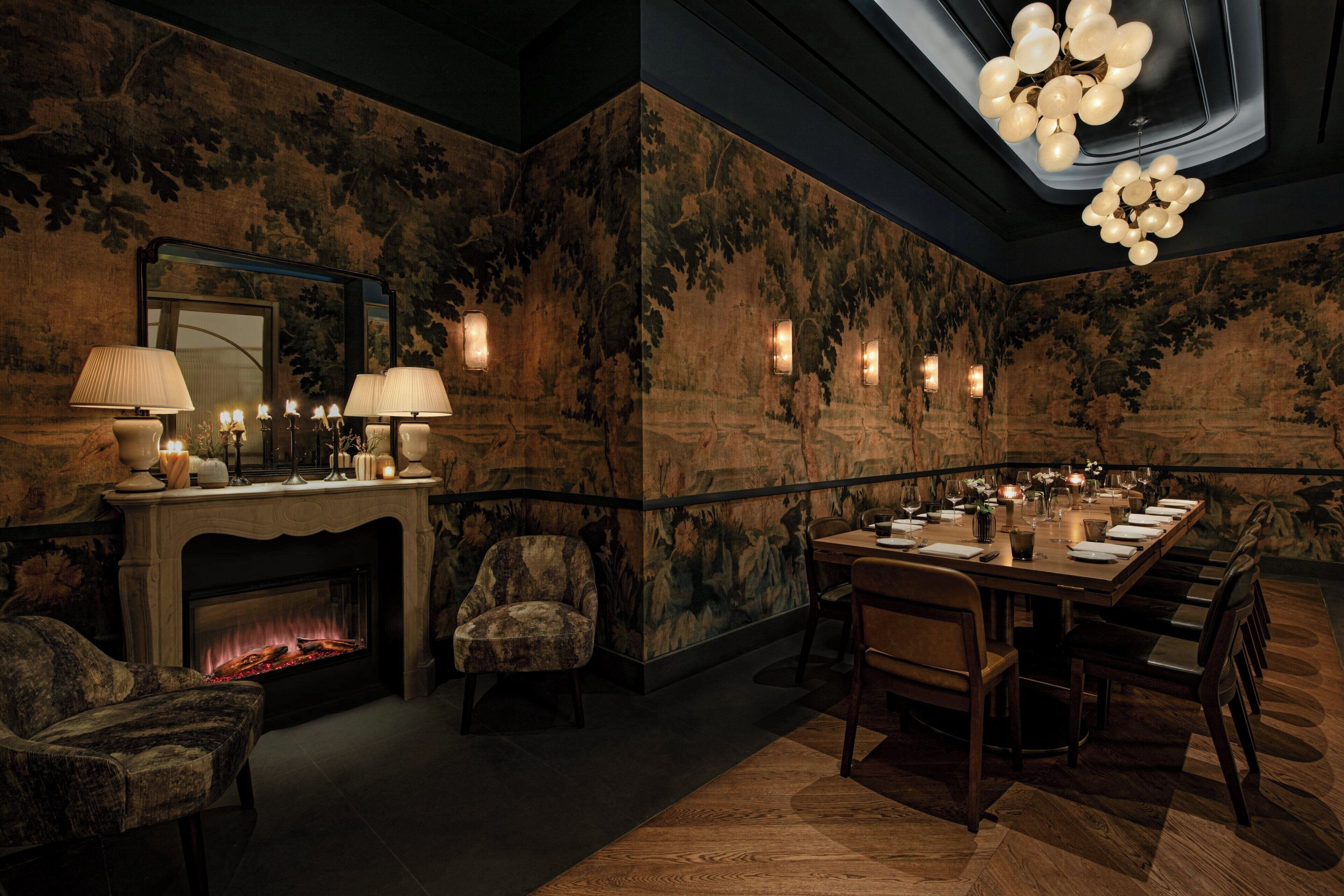 A dimly lit dining room with a fireplace, a long table set for a meal, and a patterned wall.