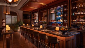 Una zona de bar con una barra larga, varios taburetes y estantes llenos de botellas.