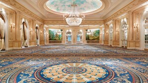 Un salón imponente con candelabros ornamentados, un amplio tapiz circular y un mural de un paisaje.