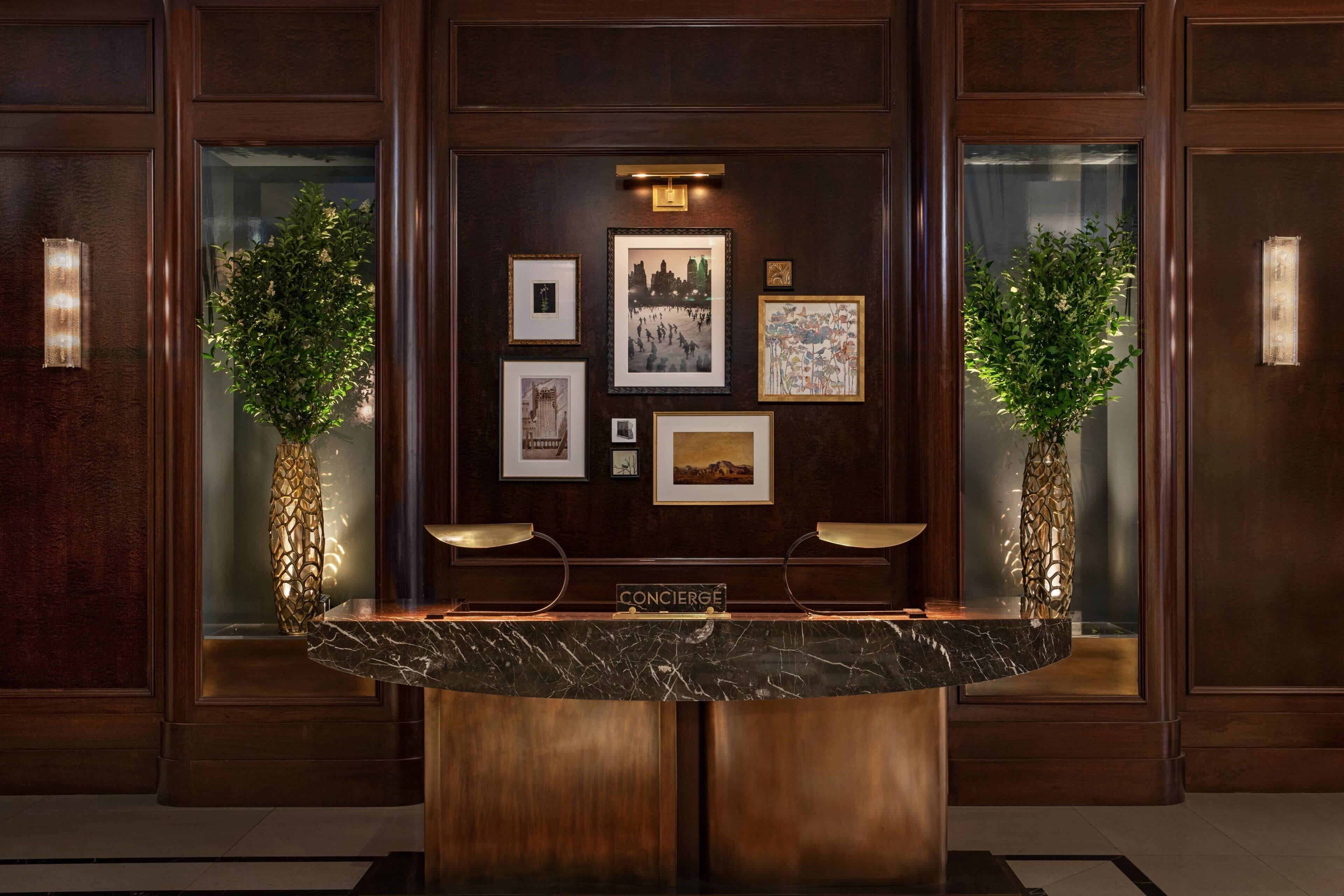 A reception desk with a marble top, framed artwork on the wall, and two potted plants.