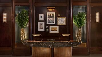 A reception desk with a marble top, framed artwork on the wall, and two potted plants.