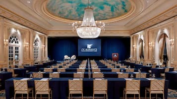 A conference room with rows of tables and chairs, a large chandelier, and a screen displaying the JW Marriott logo.