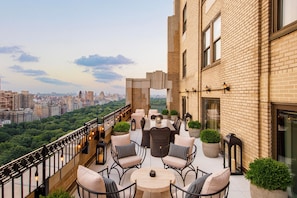 Una terraza en la azotea con mobiliario exterior, vistas a la ciudad y un edificio de ladrillo.