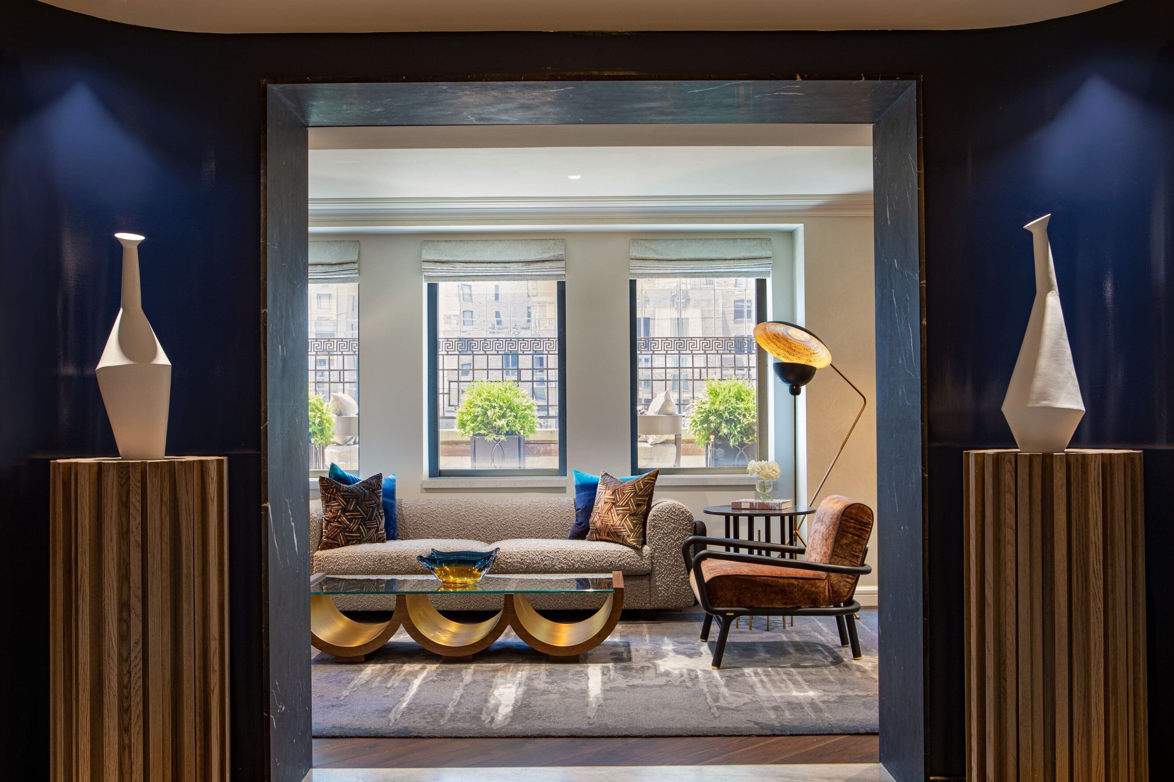 A modern living room with a sofa, armchair, and coffee table, featuring a view of the city through large windows.