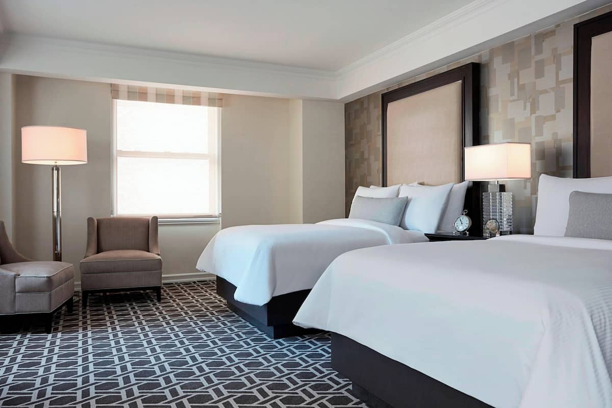 Habitación de hotel con dos camas, una silla, una lámpara de pie y una ventana.
