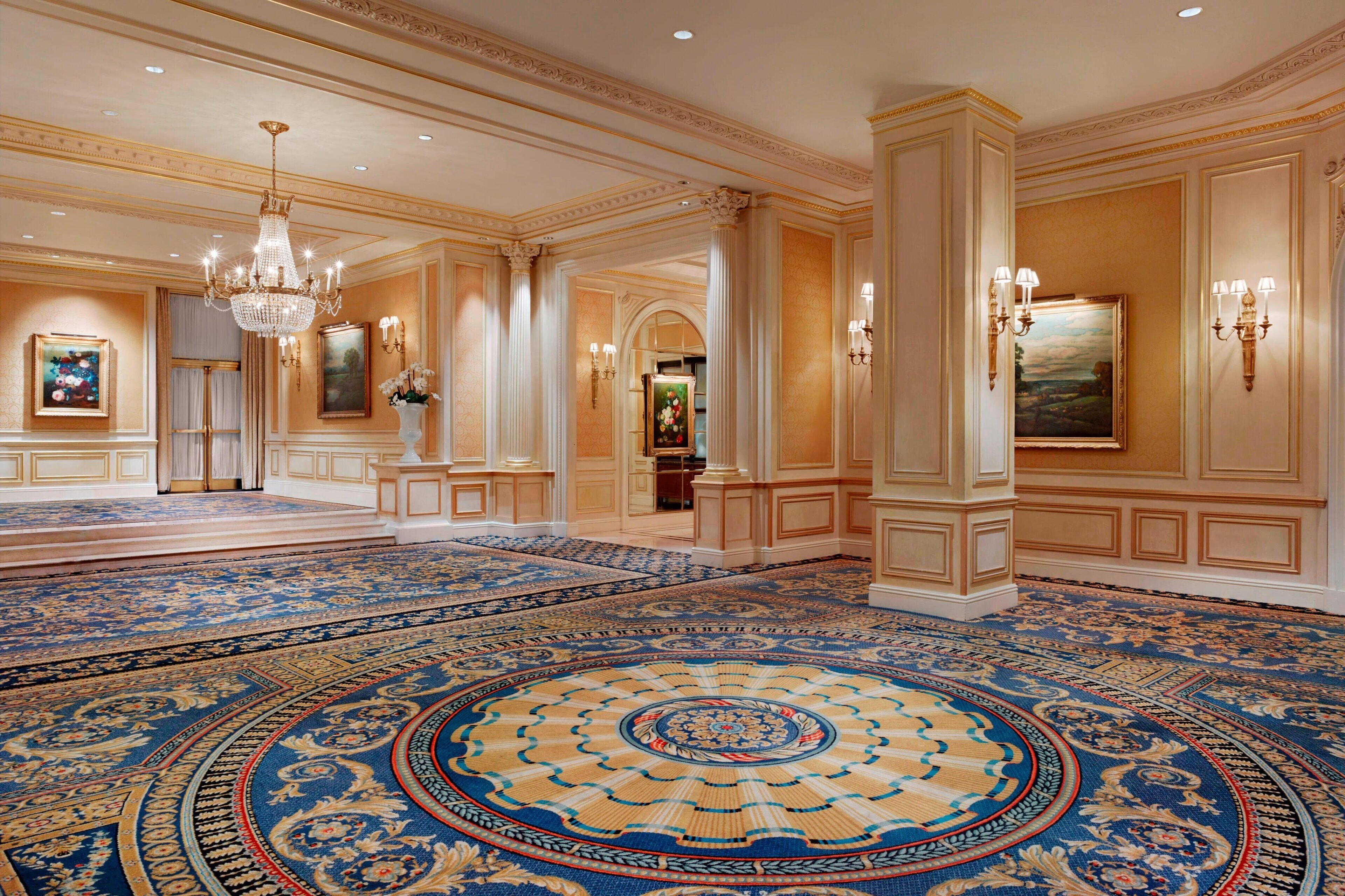 Un lobby espacioso con una alfombra grande y elaborada, candelabros y arquitectura clásica.
