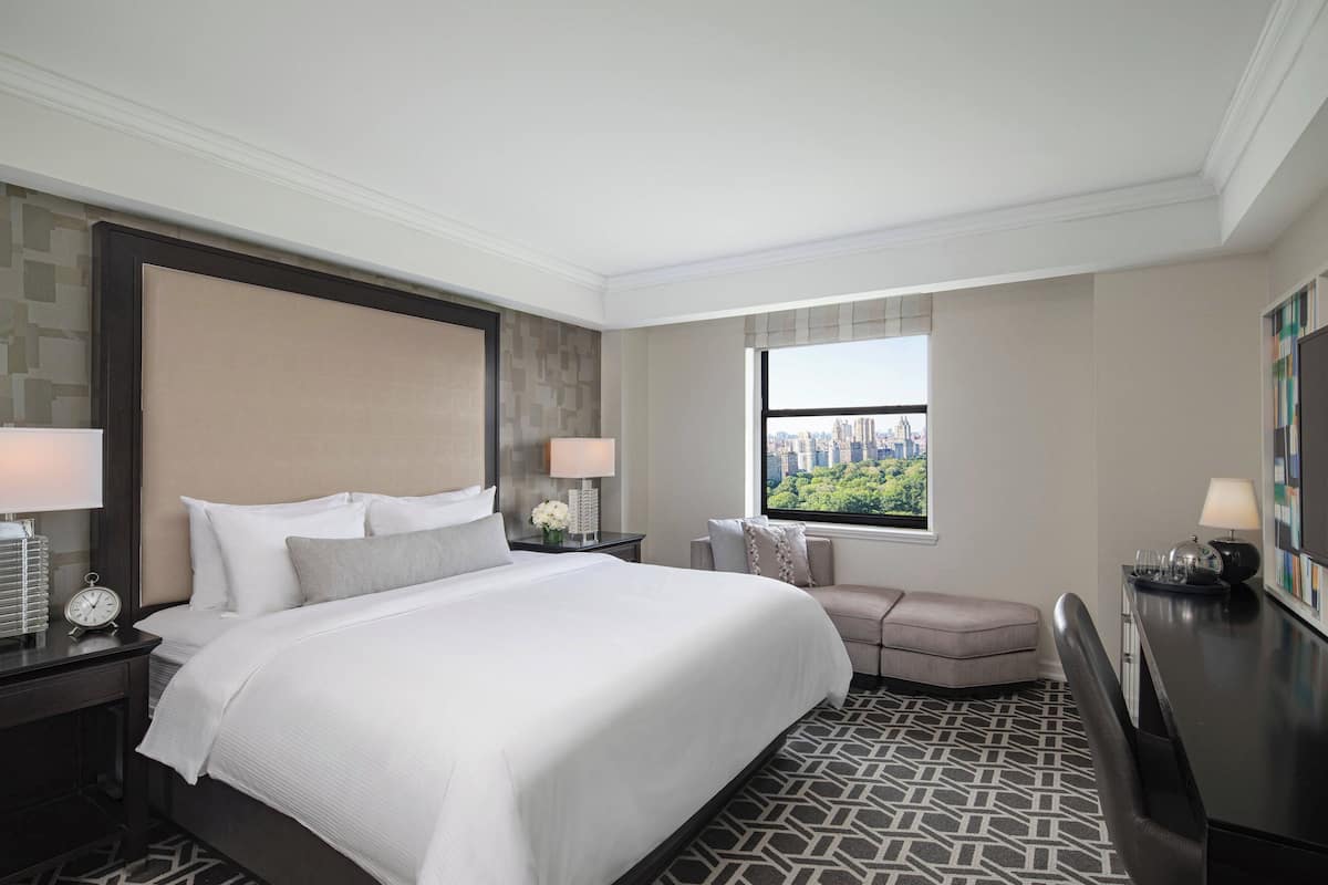 Habitación de hotel con una cama grande, un escritorio, una silla y una ventana con vista a la ciudad.