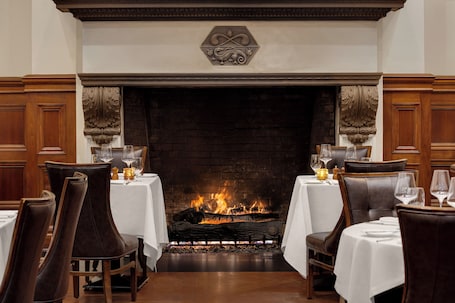 A dining area with a fireplace, wooden paneling, and tables set for dining.