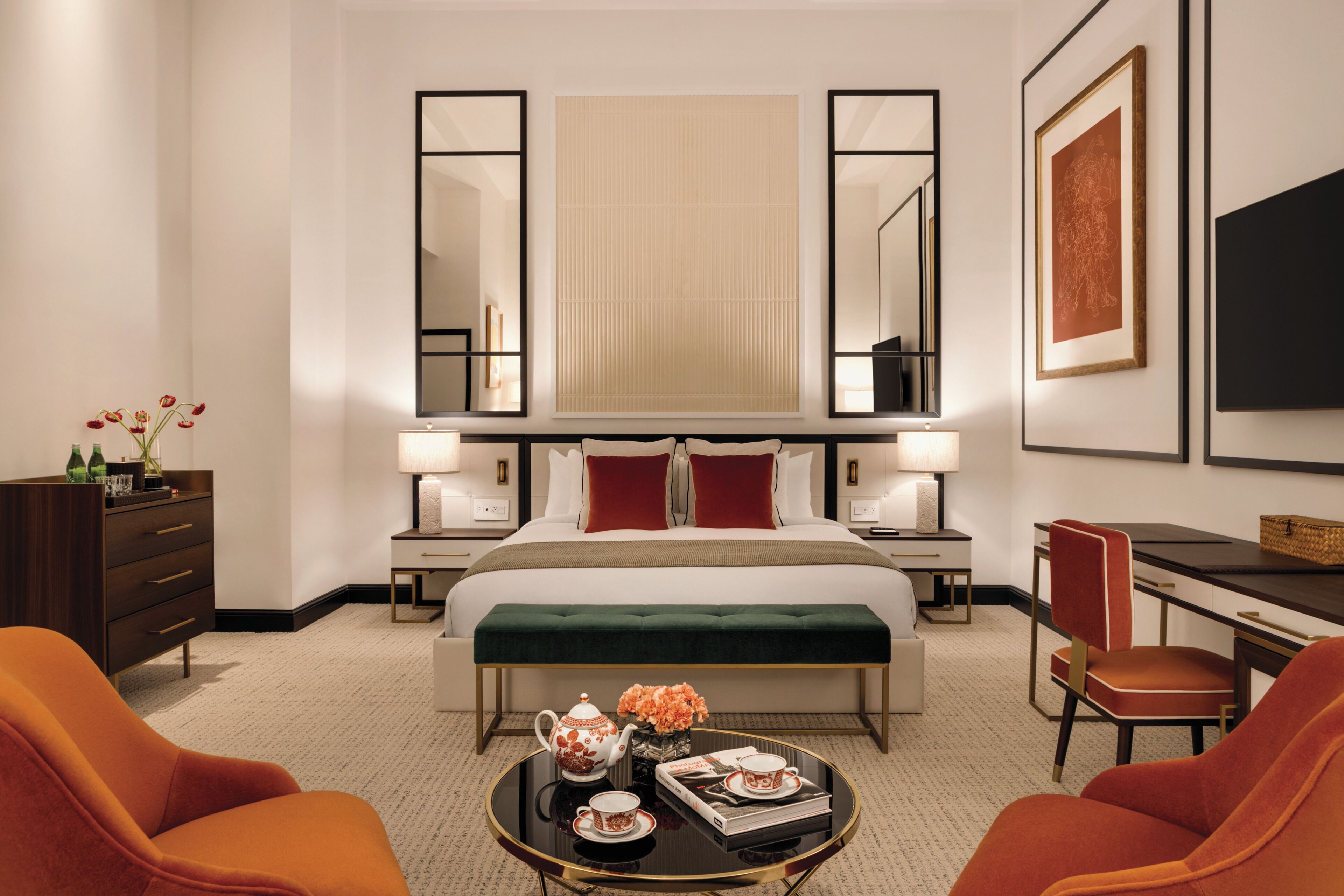 A hotel room with a large bed, two bedside tables, a desk, a chair, a round coffee table, and a TV on the wall.