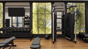 A gym with a bench, dumbbells, a squat rack, and a TV on the wall. - Eurostars The Chemists’ Club Hotel (New York)