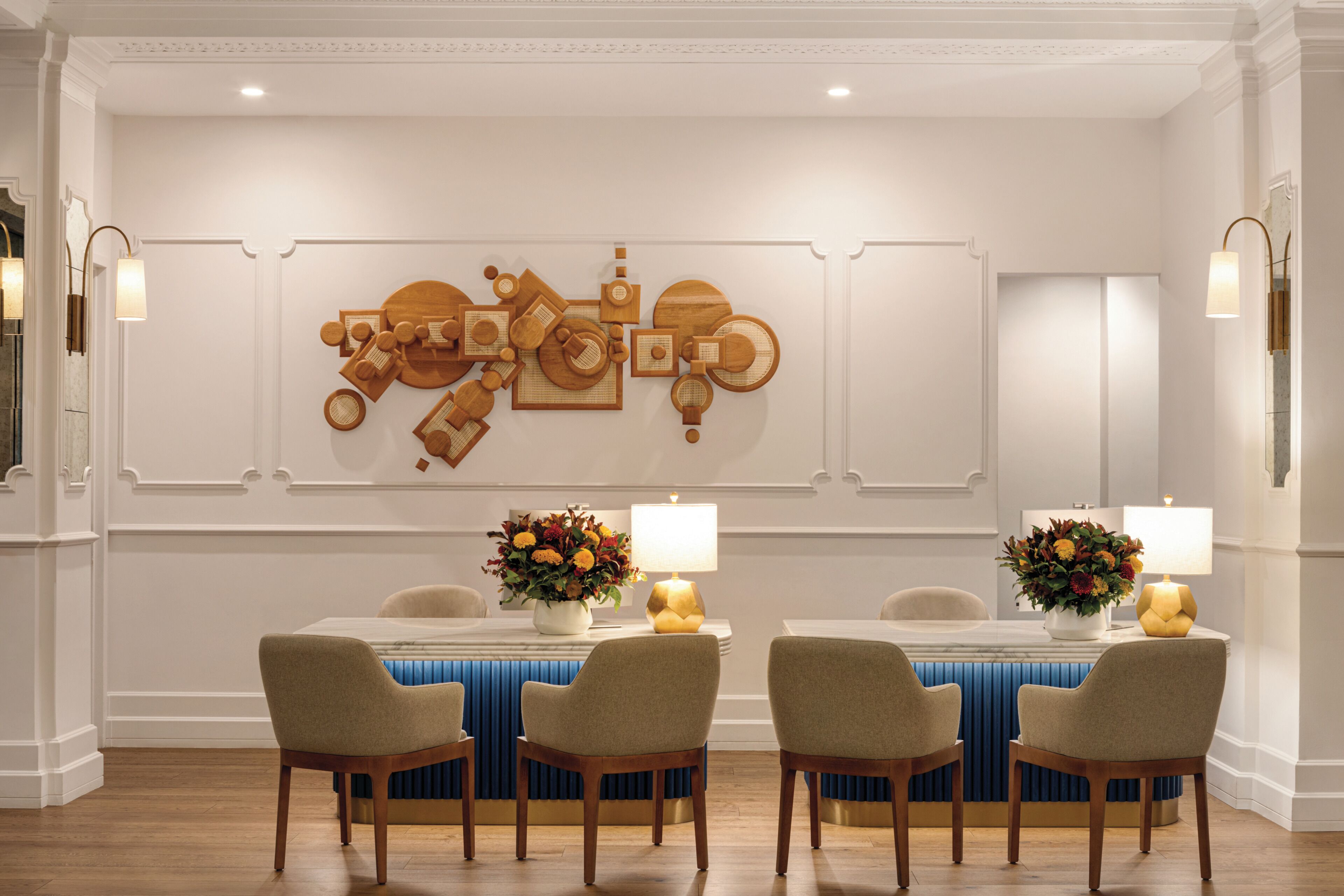 A dining area with a white table, four chairs, and wall-mounted lamps.