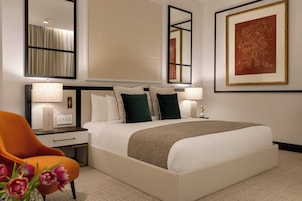 A hotel room with a bed, bedside lamps, a chair, and a large framed artwork on the wall.