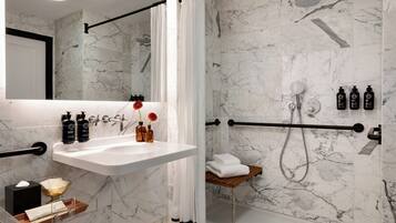 A modern bathroom with a marble shower, a white sink, and toiletries.
