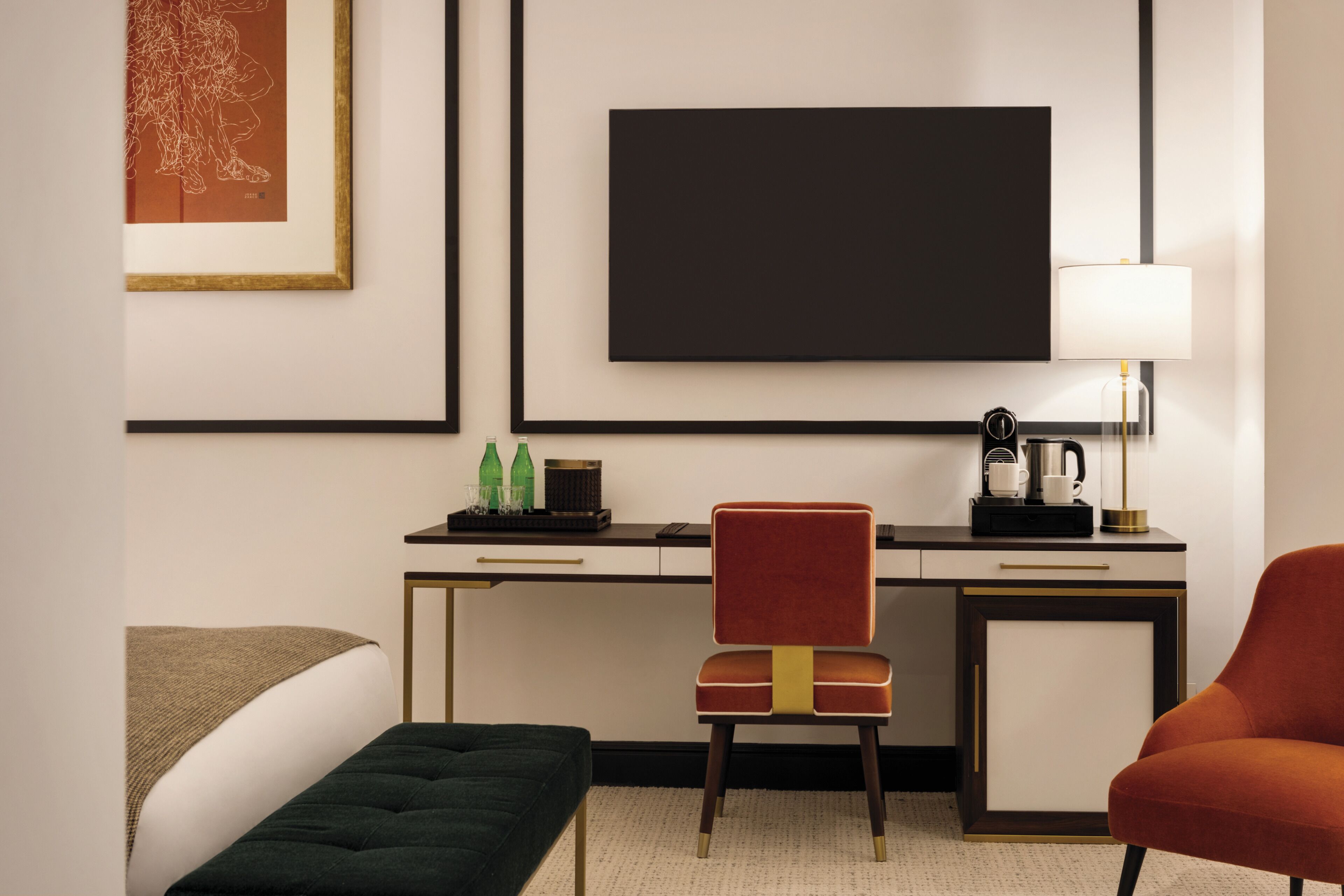 A hotel room with a bed, a desk with a chair, a coffee maker, and a lamp.