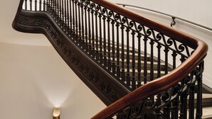 A spiral staircase with ornate black balusters and a wooden handrail. - Eurostars The Chemists’ Club Hotel (New York)