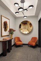 Un interior moderno con una lámpara de techo, una obra de arte enmarcada, un jarrón con flores y dos sillones anaranjados.