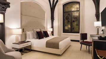 Habitación de hotel con una cama grande, un escritorio, una silla y un ventanal con vidrieras.
